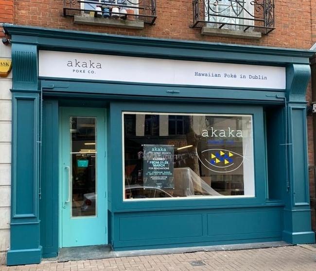 Street view of the teal-colored storefront for "Akaka Poke Co.", a Hawaiian poké restaurant in Dublin, with a large window and sign above the door reading “Hawaiian Poké in Dublin”.