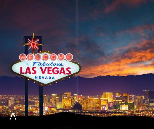 The iconic 'Welcome to Fabulous Las Vegas, Nevada' sign illuminated at dusk, with the brightly lit Las Vegas Strip and dramatic sunset clouds in the background.
