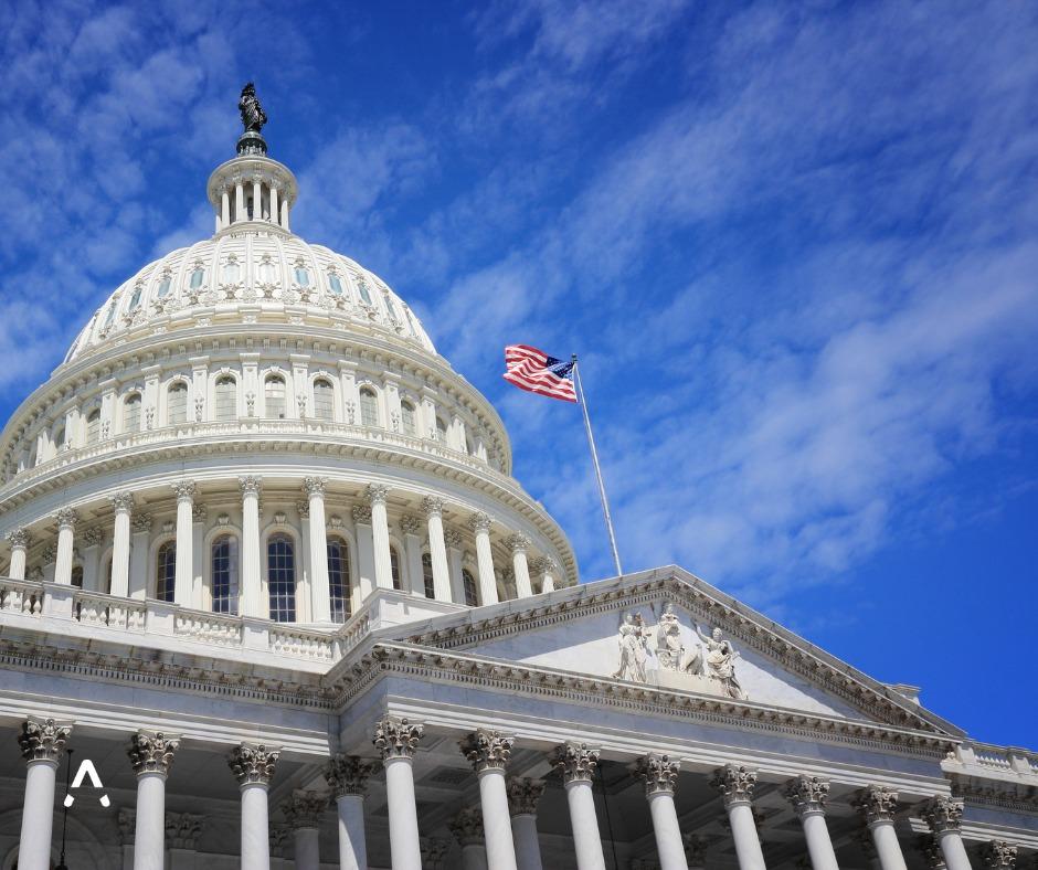 Close-up view of the U.S. Capitol building's dome and facade in Washington, D.C., with the American flag flying against a bright blue sky with scattered clouds.