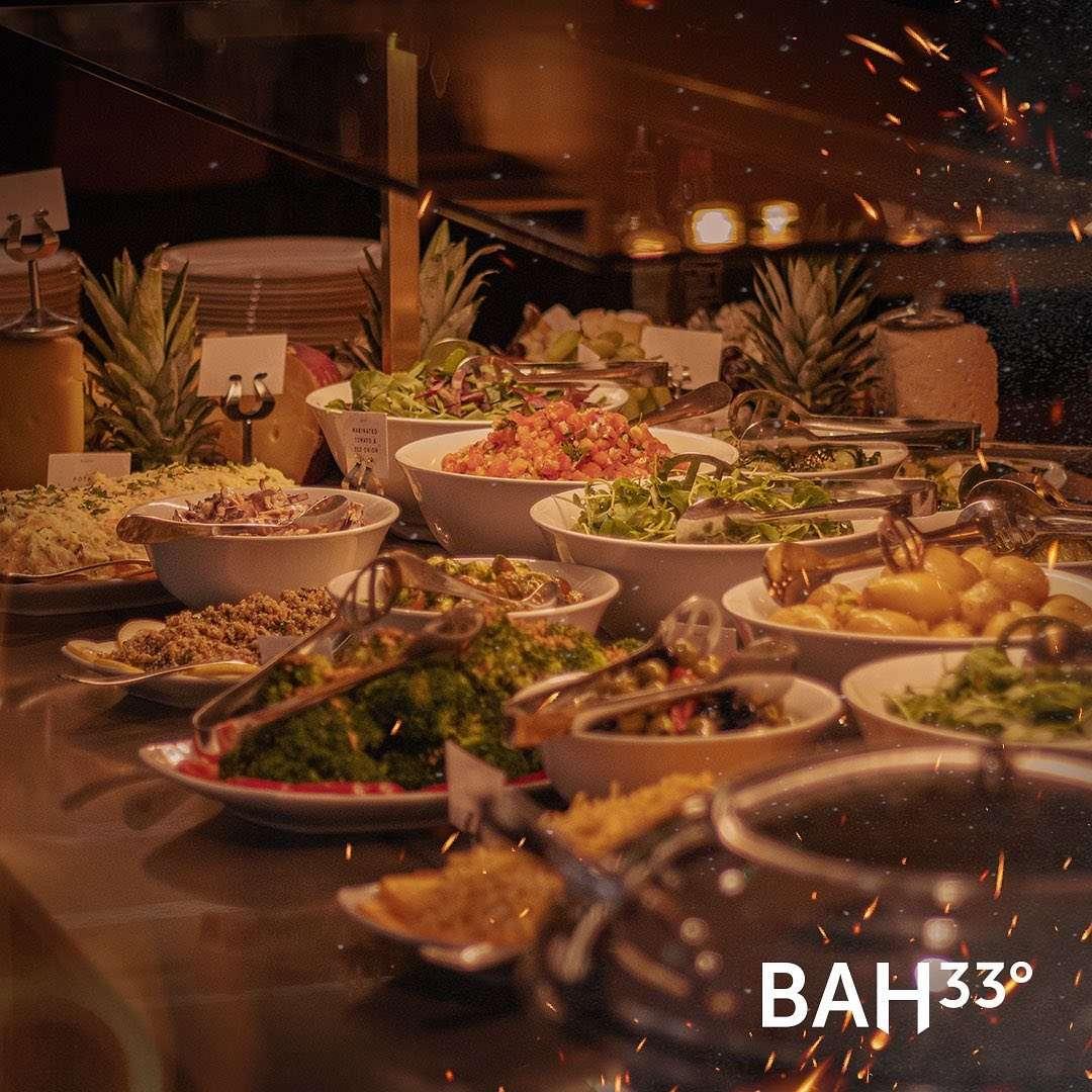 A buffet display featuring an assortment of fresh salads, vegetables, and side dishes served in white bowls, with tongs for self-service. The warm lighting and decorative pineapples in the background add to the inviting atmosphere.