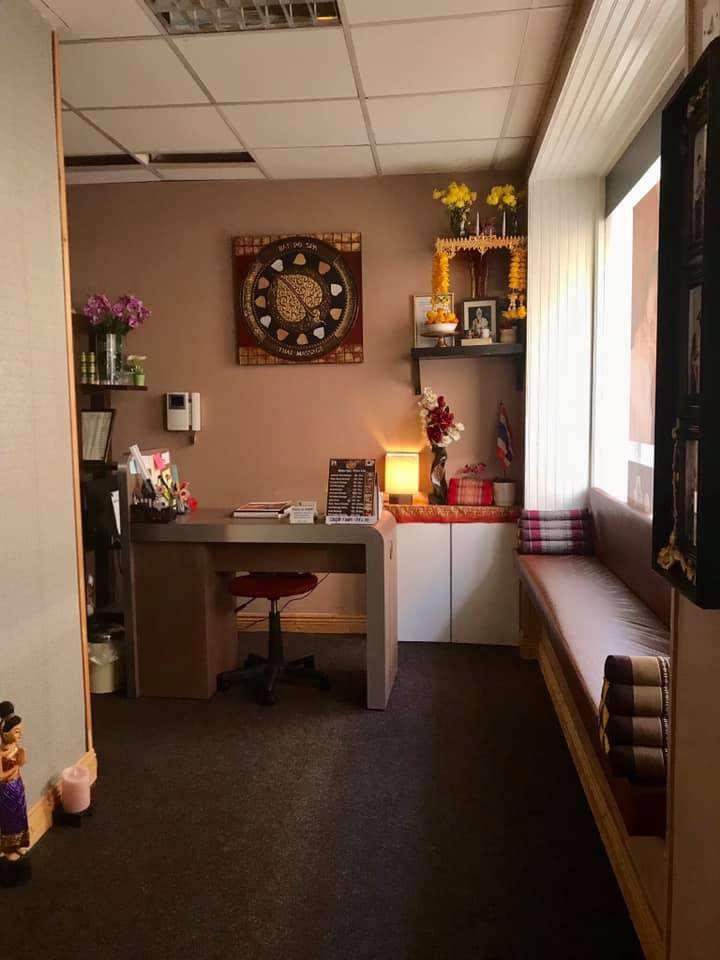 Small office area with a desk, chair, and shelves decorated with flowers and a wall clock. A cushioned bench with pillows is by the window.
