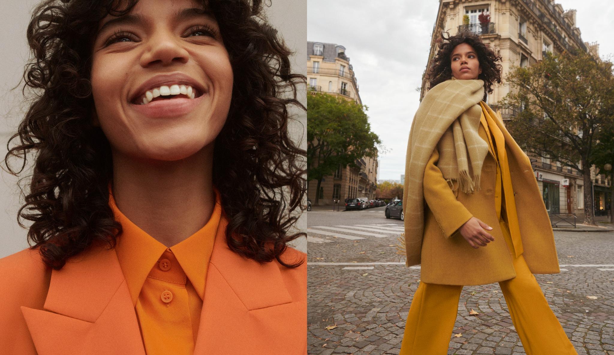 A fashion model wearing bold, monochromatic outfits in warm tones. On the left, she smiles brightly in a close-up shot, dressed in a vibrant orange suit. On the right, she strides confidently through a Parisian street wearing a mustard yellow coat and pants, layered with a beige plaid scarf. The backdrop features classic Paris architecture and autumn trees.
